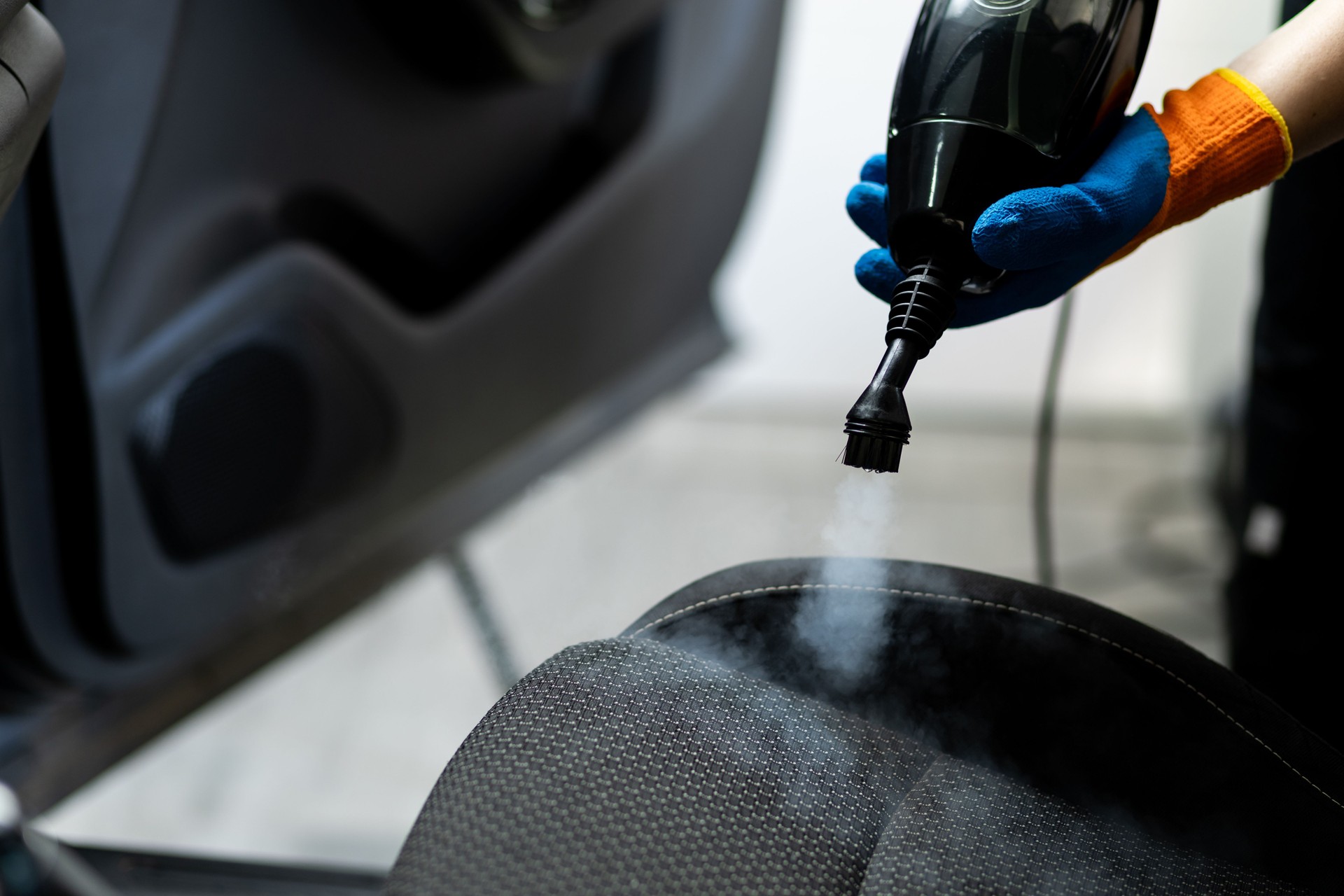 Nettoyage à la vapeur des tissus d’ameublement d’une voiture lors d’une séance d’esthétique automobile dans un atelier de réparation automobile