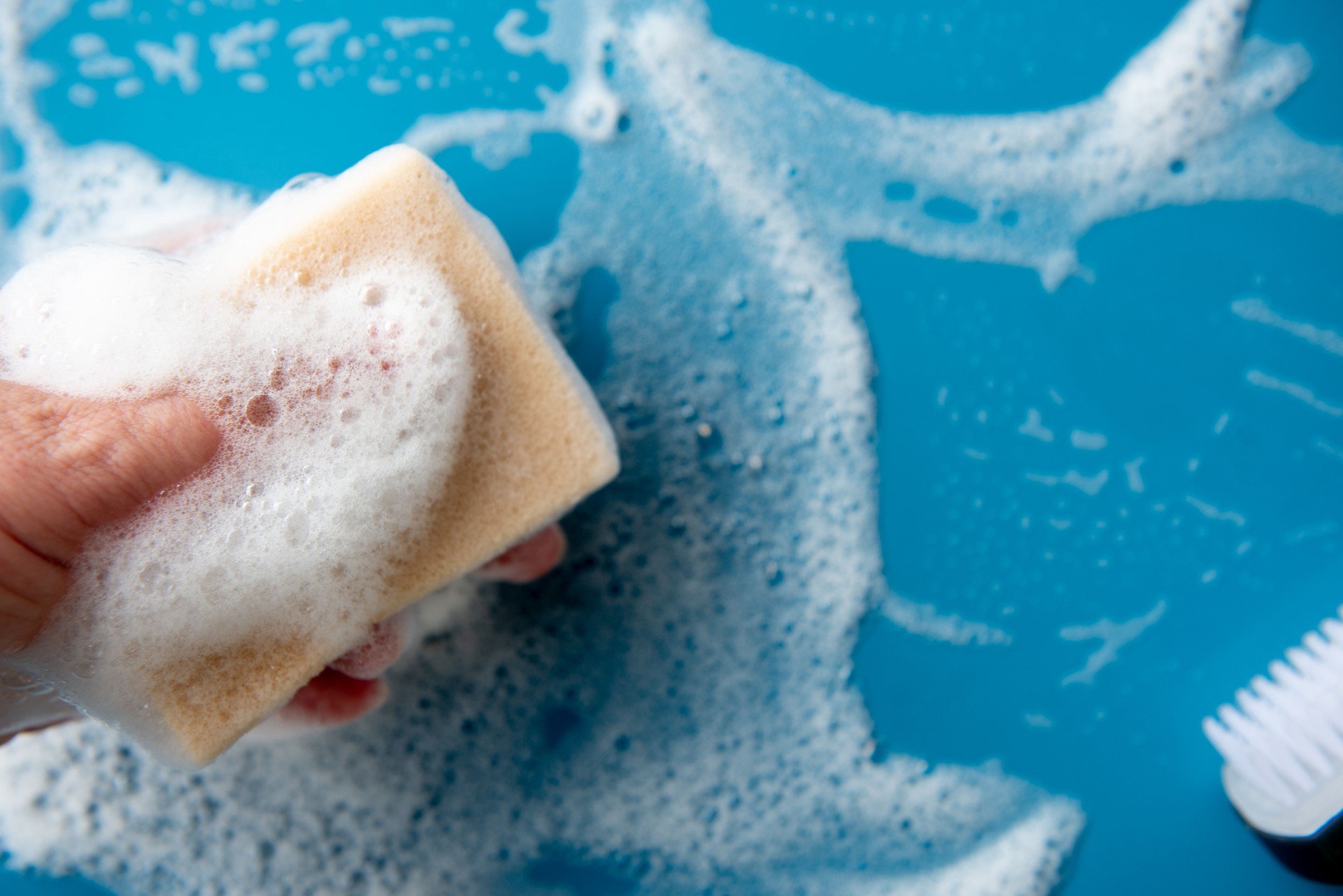 Hand holds a cleaning sponge and wipes a soapy foam on a blue tile.